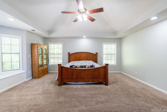 carpeted bedroom with vaulted ceiling, ceiling fan, a tray ceiling, and a textured ceiling