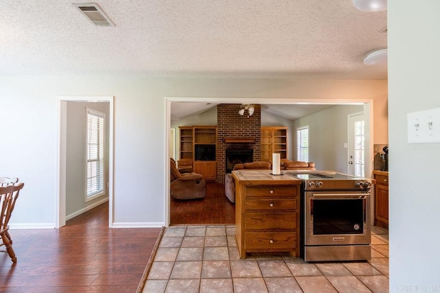 kitchen with high end range, a healthy amount of sunlight, light tile floors, and a brick fireplace