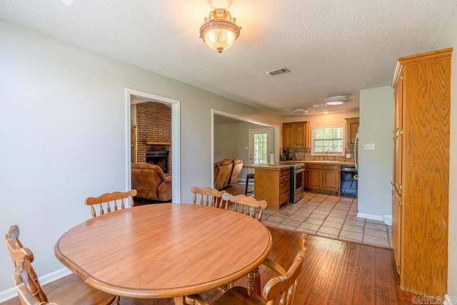 dining area with sink, a brick fireplace, light wood-type flooring, and a textured ceiling