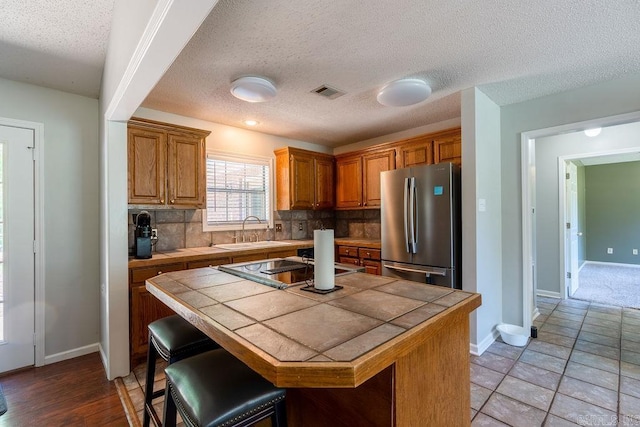 kitchen featuring backsplash, a kitchen island, stainless steel refrigerator, sink, and a breakfast bar