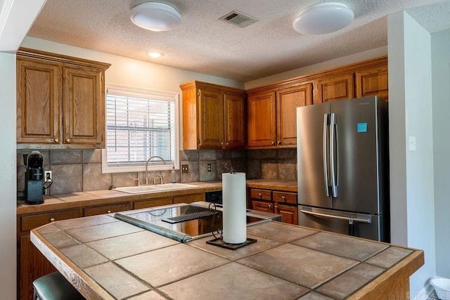 kitchen with stainless steel refrigerator, tile counters, and backsplash