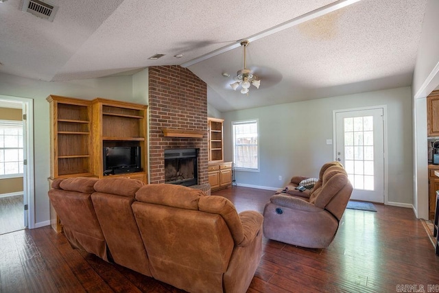 living room with ceiling fan, vaulted ceiling, brick wall, a fireplace, and dark hardwood / wood-style flooring