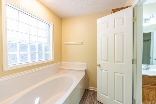 bathroom featuring a textured ceiling, hardwood / wood-style floors, vanity, and a bathing tub