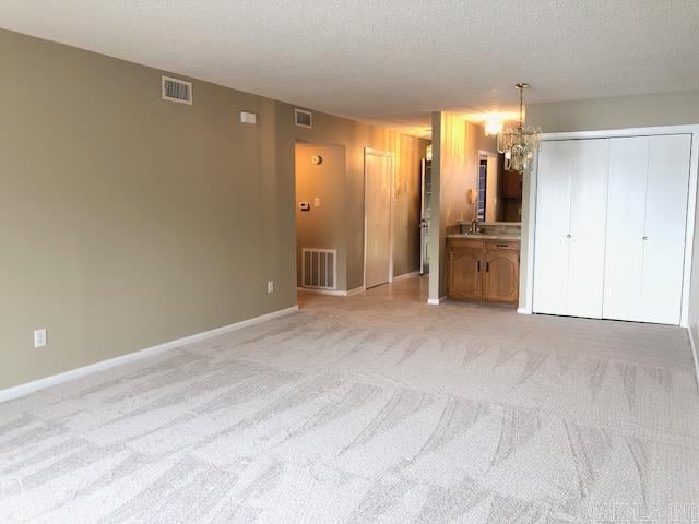 unfurnished bedroom featuring ensuite bath, light colored carpet, a textured ceiling, and a notable chandelier