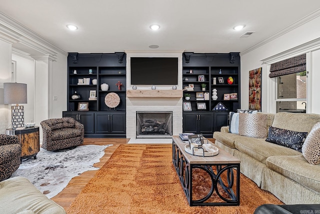 living room featuring built in features, a large fireplace, light hardwood / wood-style flooring, and ornamental molding