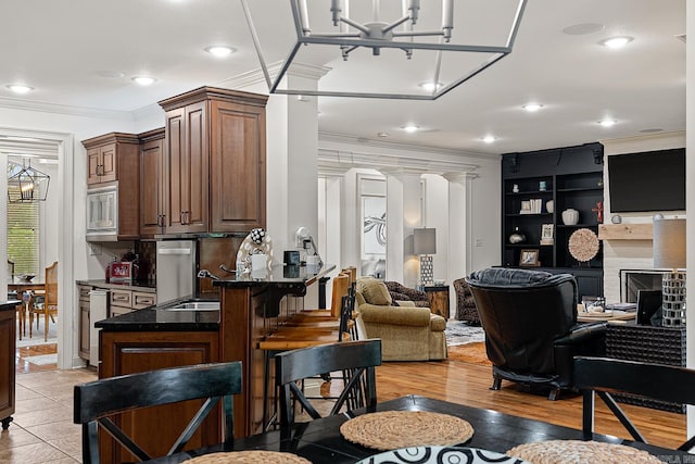 interior space featuring sink, stainless steel microwave, decorative columns, ornamental molding, and an inviting chandelier