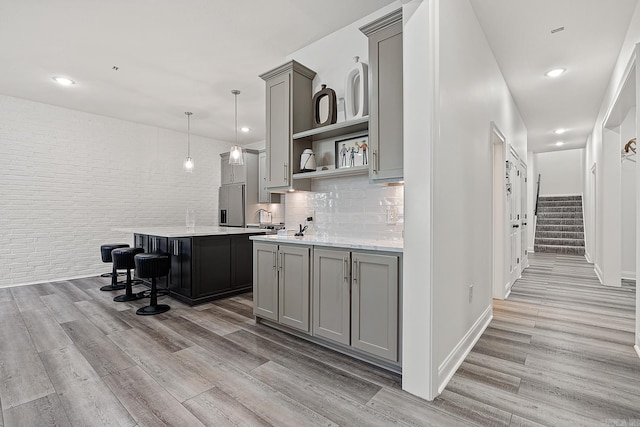 kitchen featuring light hardwood / wood-style floors, tasteful backsplash, hanging light fixtures, a center island with sink, and stainless steel refrigerator with ice dispenser