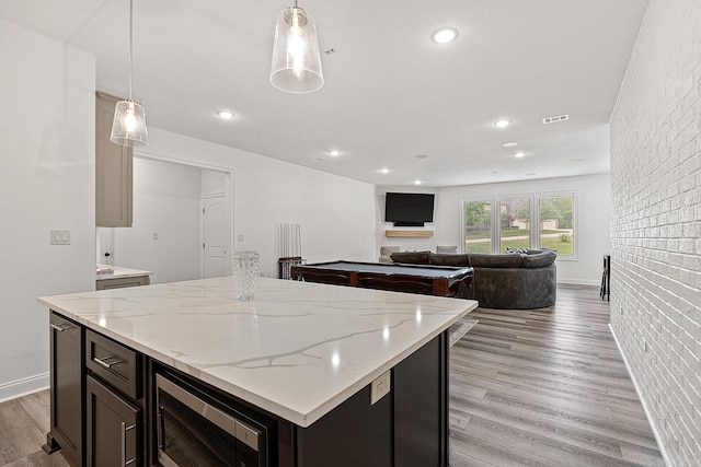 kitchen featuring decorative light fixtures, billiards, light hardwood / wood-style floors, brick wall, and a center island