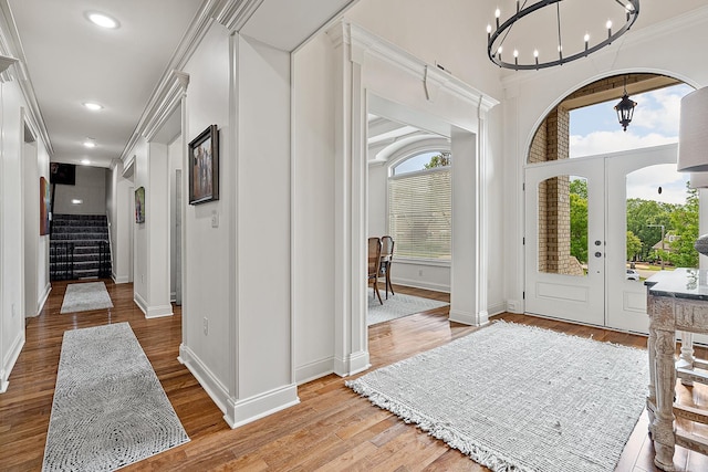 foyer featuring french doors, crown molding, light wood-type flooring, and an inviting chandelier