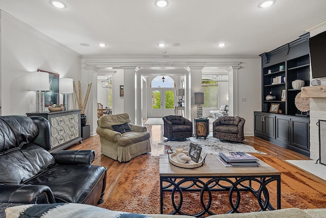 living room featuring ornamental molding, wood-type flooring, decorative columns, and built in shelves