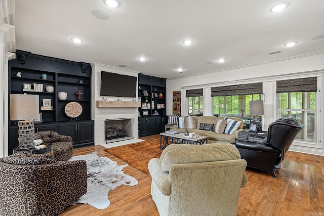 living room with a fireplace, light hardwood / wood-style floors, built in features, and crown molding