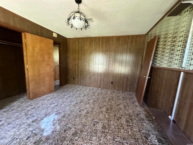 unfurnished bedroom featuring a closet, a textured ceiling, wood walls, and carpet flooring