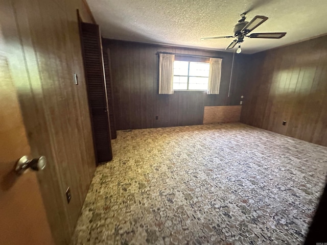 unfurnished room with a textured ceiling, wood walls, ceiling fan, and carpet