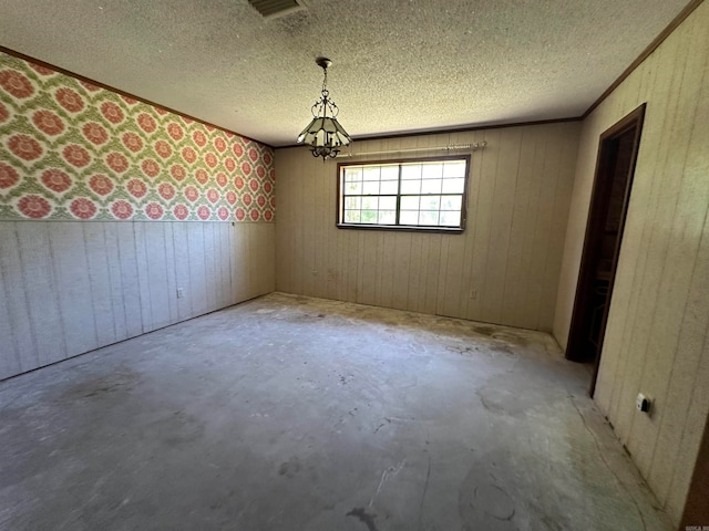 spare room with an inviting chandelier, wood walls, concrete floors, and a textured ceiling