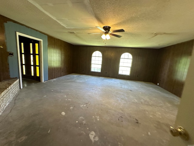 unfurnished room with a textured ceiling, wood walls, ceiling fan, and concrete floors