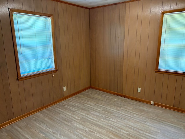 empty room with light hardwood / wood-style floors, wooden walls, and a wealth of natural light