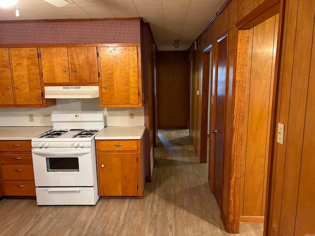 kitchen featuring light hardwood / wood-style flooring, wooden walls, and gas range gas stove