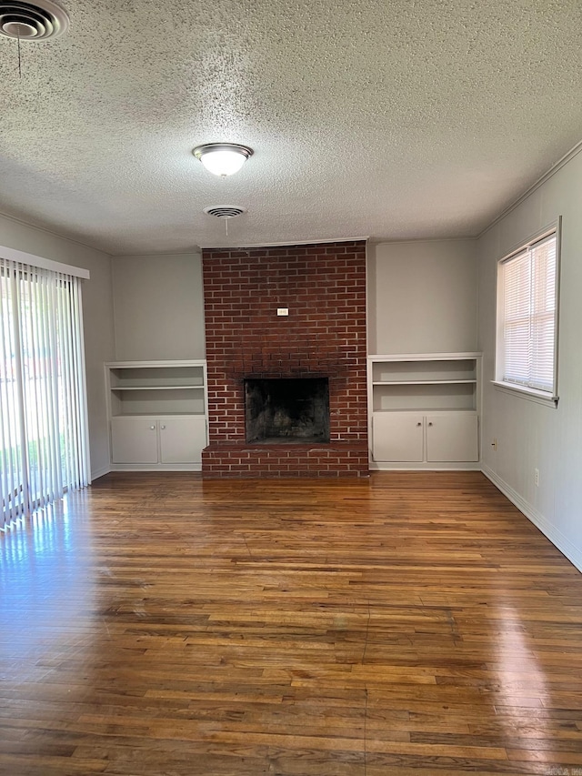 unfurnished living room with a healthy amount of sunlight, dark wood-type flooring, brick wall, and a brick fireplace