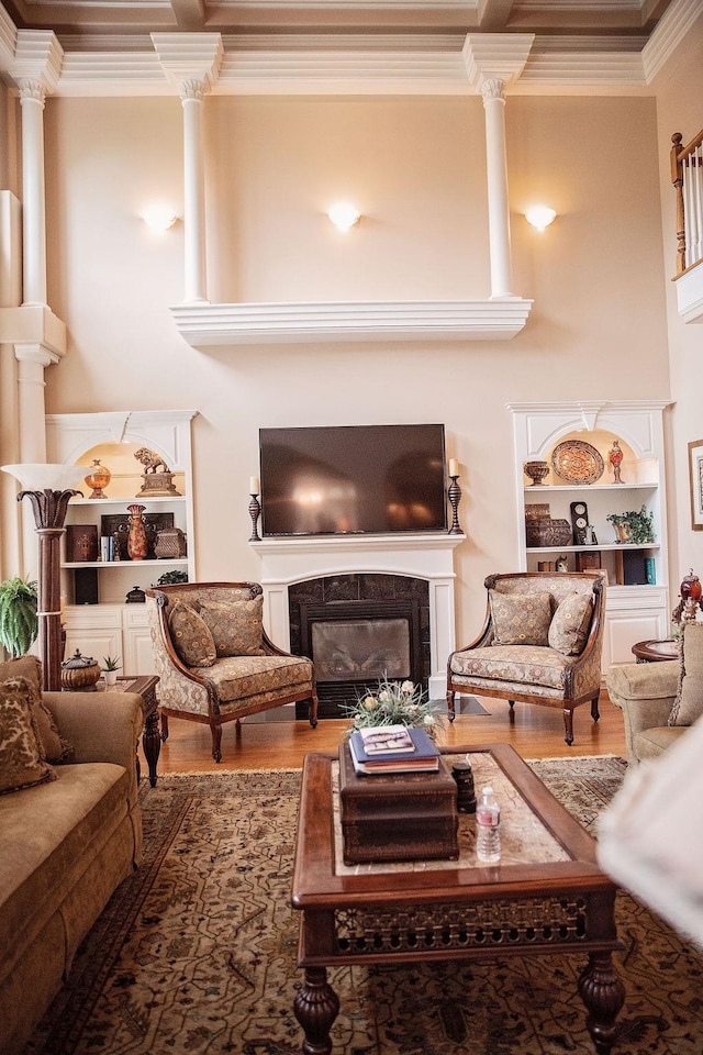 living room featuring a tiled fireplace, hardwood / wood-style flooring, ornamental molding, built in shelves, and decorative columns