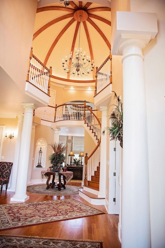 entryway featuring a notable chandelier, hardwood / wood-style flooring, crown molding, a high ceiling, and decorative columns