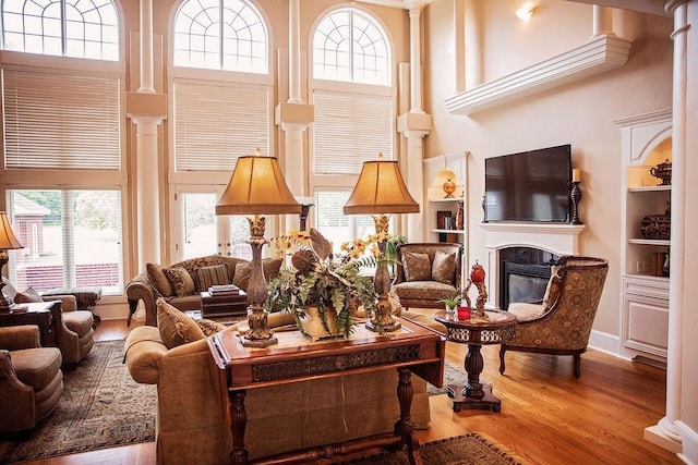 living room featuring a high ceiling, built in shelves, hardwood / wood-style flooring, and decorative columns