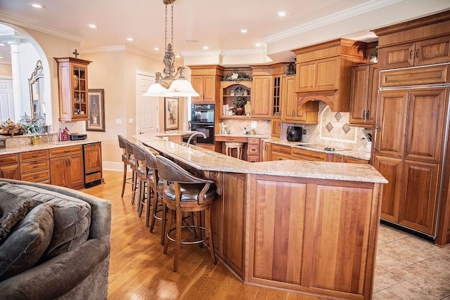 kitchen featuring light stone countertops, light hardwood / wood-style floors, an island with sink, black appliances, and backsplash