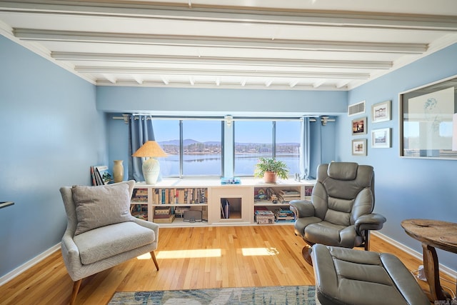 living area with beamed ceiling, a water view, hardwood / wood-style flooring, and ornamental molding