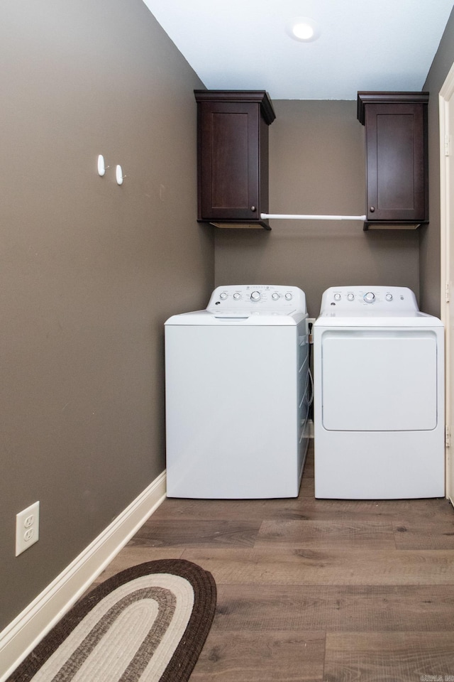 washroom featuring washing machine and clothes dryer, hardwood / wood-style flooring, and cabinets