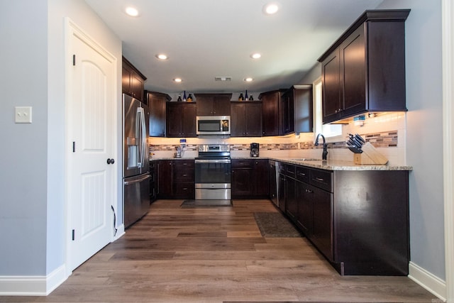 kitchen with decorative backsplash, appliances with stainless steel finishes, light stone countertops, wood-type flooring, and sink