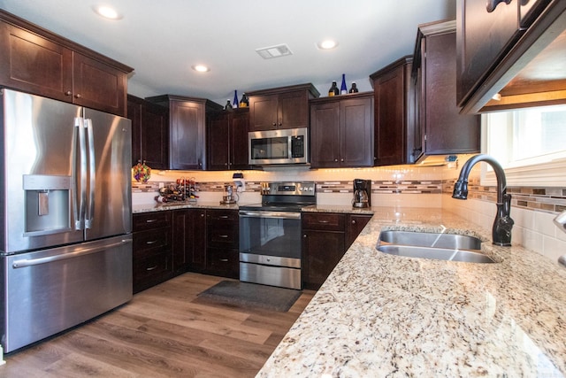 kitchen featuring dark brown cabinets, stainless steel appliances, sink, light stone countertops, and light hardwood / wood-style floors