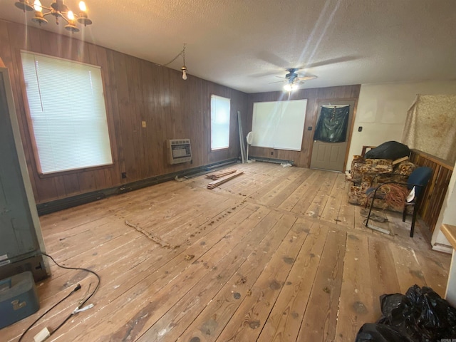 interior space featuring wooden walls, a wall mounted air conditioner, ceiling fan with notable chandelier, light hardwood / wood-style floors, and a textured ceiling