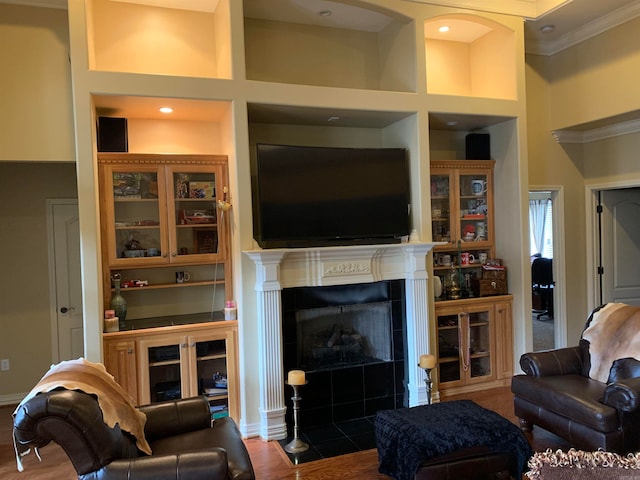 living room with hardwood / wood-style flooring, a tiled fireplace, built in shelves, and a towering ceiling