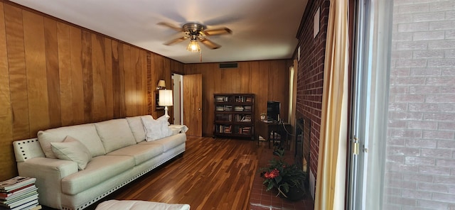 living room featuring ceiling fan, a brick fireplace, brick wall, dark hardwood / wood-style floors, and wood walls