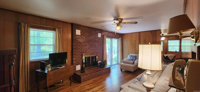 living room featuring hardwood / wood-style floors, ceiling fan, a fireplace, and wood walls