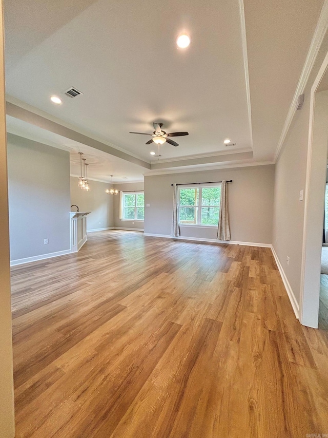 unfurnished living room featuring ceiling fan with notable chandelier, ornamental molding, light hardwood / wood-style floors, and a raised ceiling