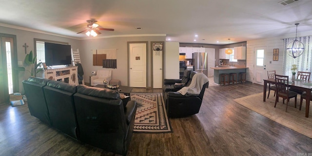 living room featuring ceiling fan with notable chandelier, a wealth of natural light, dark wood-type flooring, and ornamental molding