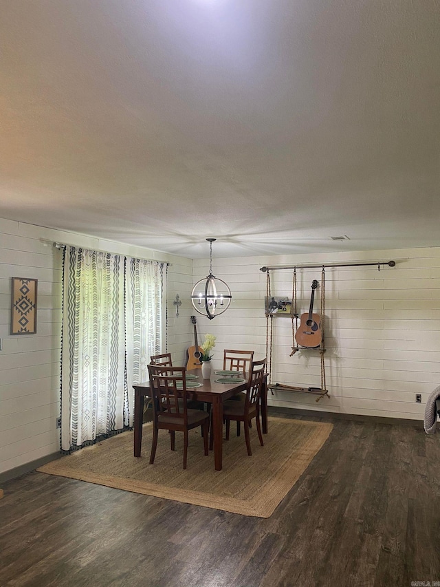 dining space featuring wood walls, dark wood-type flooring, and a chandelier