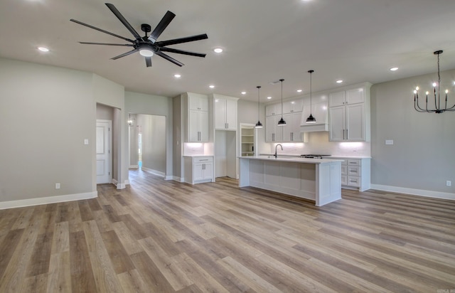 kitchen with pendant lighting, ceiling fan with notable chandelier, a large island, and light hardwood / wood-style flooring