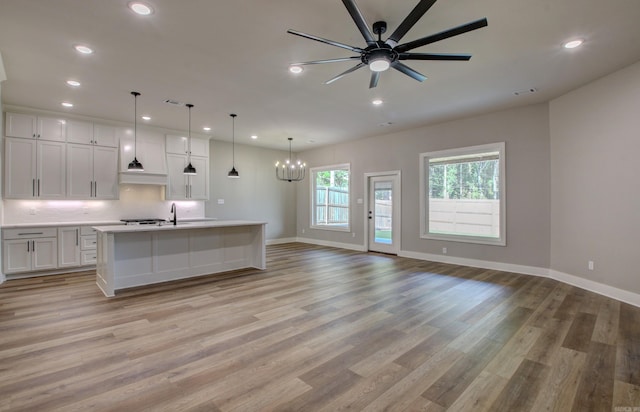 kitchen featuring ceiling fan with notable chandelier, an island with sink, hanging light fixtures, white cabinets, and light hardwood / wood-style floors