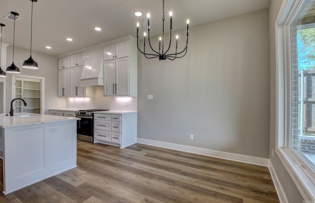 kitchen with white cabinets, custom exhaust hood, light hardwood / wood-style floors, stainless steel gas range, and pendant lighting