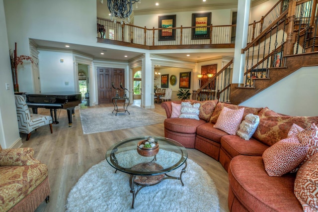 living room featuring decorative columns, ornamental molding, a towering ceiling, a notable chandelier, and hardwood / wood-style flooring