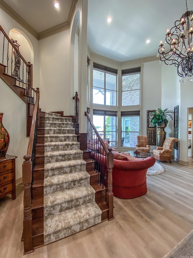 staircase with a high ceiling, hardwood / wood-style flooring, a chandelier, and ornamental molding