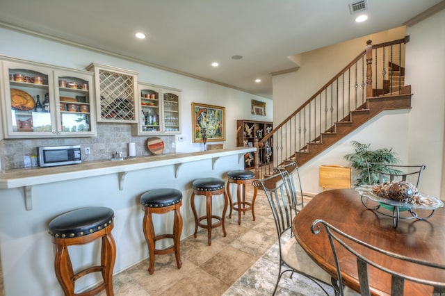 kitchen featuring tasteful backsplash, ornamental molding, light tile floors, and a kitchen bar