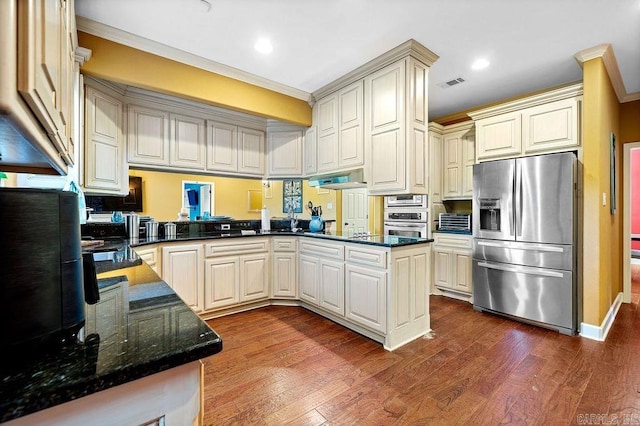 kitchen with dark stone counters, hardwood / wood-style floors, crown molding, stainless steel appliances, and kitchen peninsula