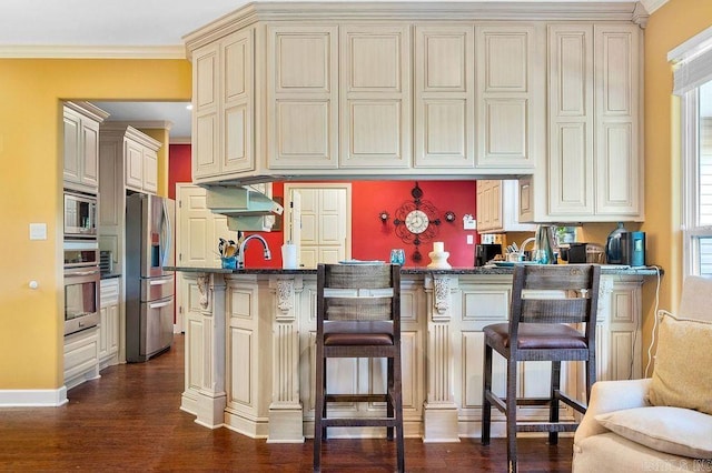 kitchen featuring cream cabinets, stainless steel appliances, dark wood-type flooring, and a breakfast bar