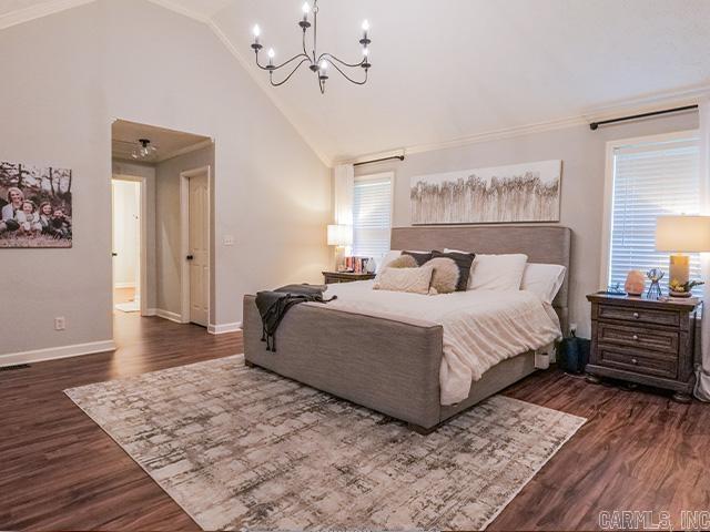 bedroom featuring ensuite bathroom, high vaulted ceiling, dark wood-type flooring, a chandelier, and ornamental molding