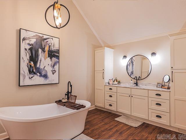 bathroom featuring a bath to relax in, vanity, hardwood / wood-style floors, ornamental molding, and vaulted ceiling