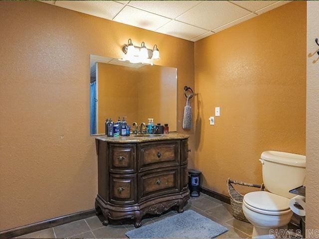 bathroom with tile flooring, a drop ceiling, vanity, and toilet