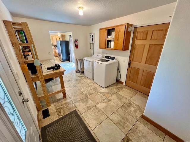 clothes washing area with washer and clothes dryer, a textured ceiling, cabinets, and light tile floors