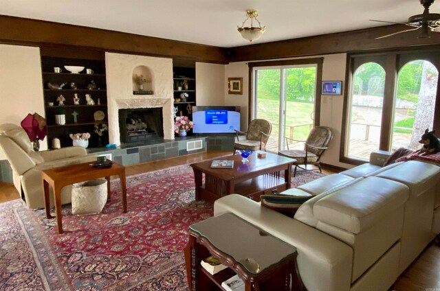 living room with a wealth of natural light, a fireplace, built in features, hardwood / wood-style floors, and ceiling fan